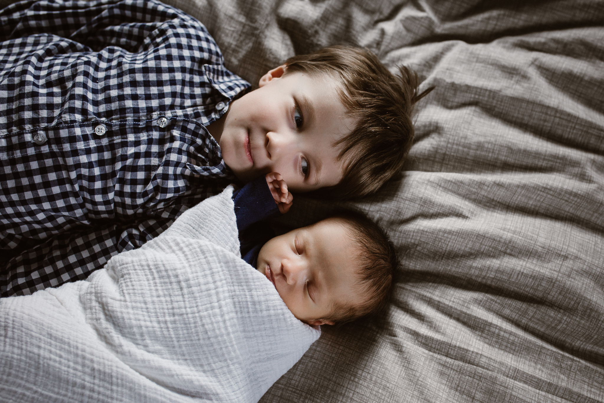 Newborn baby girl touching her brother's face on the bed.