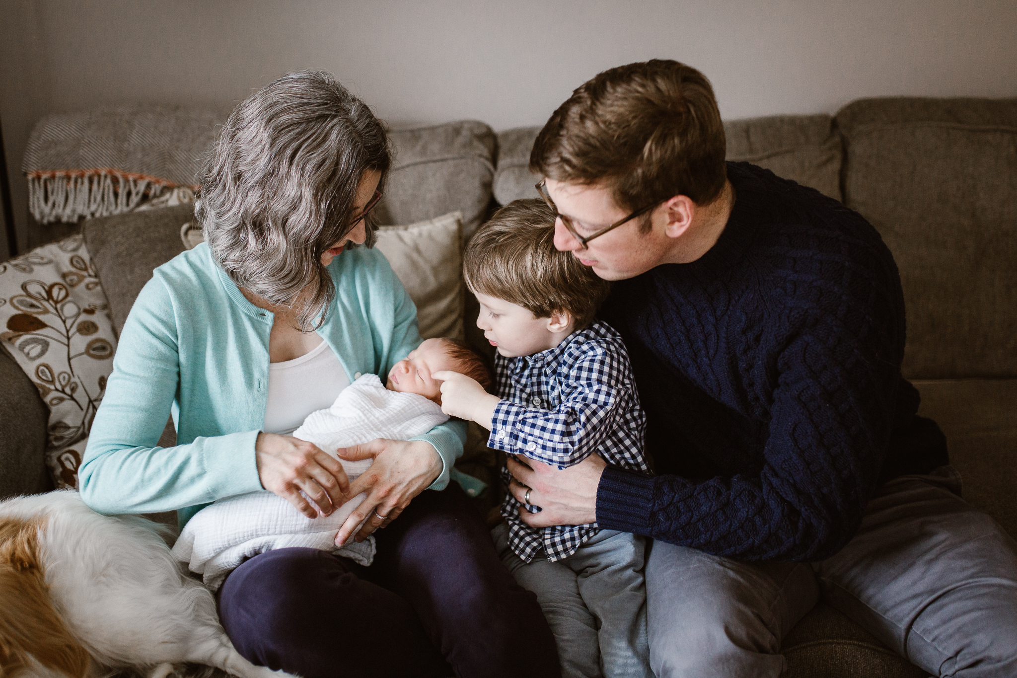 Big brother touching baby sister's face with his mother and father on the couch.