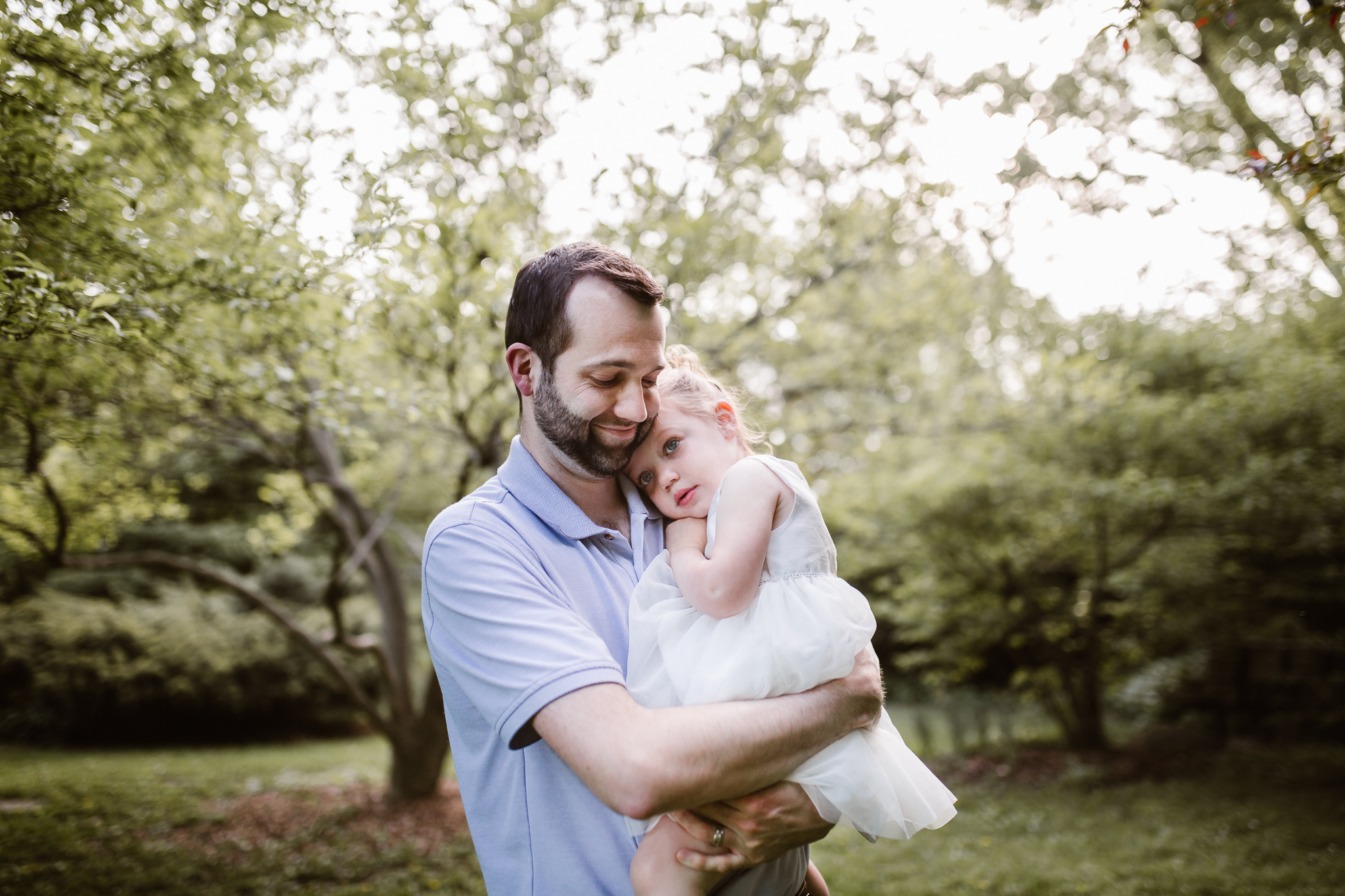 Father holder his yound daughter lovingly while snuggling her near the magnolia tree.