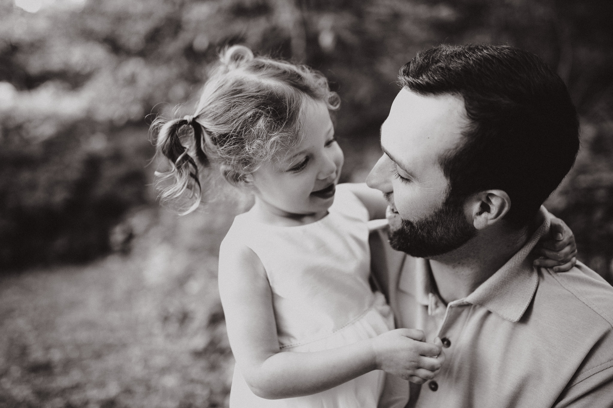 A sweet moment with a father and young daughter looking at each other outdoors.