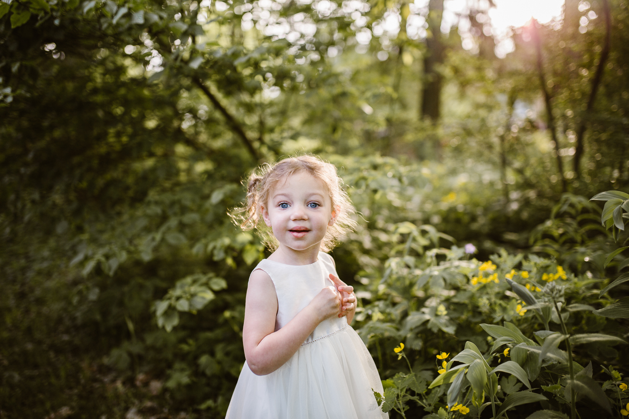 Young girl looking at flowers with the sunset shining through the trees.