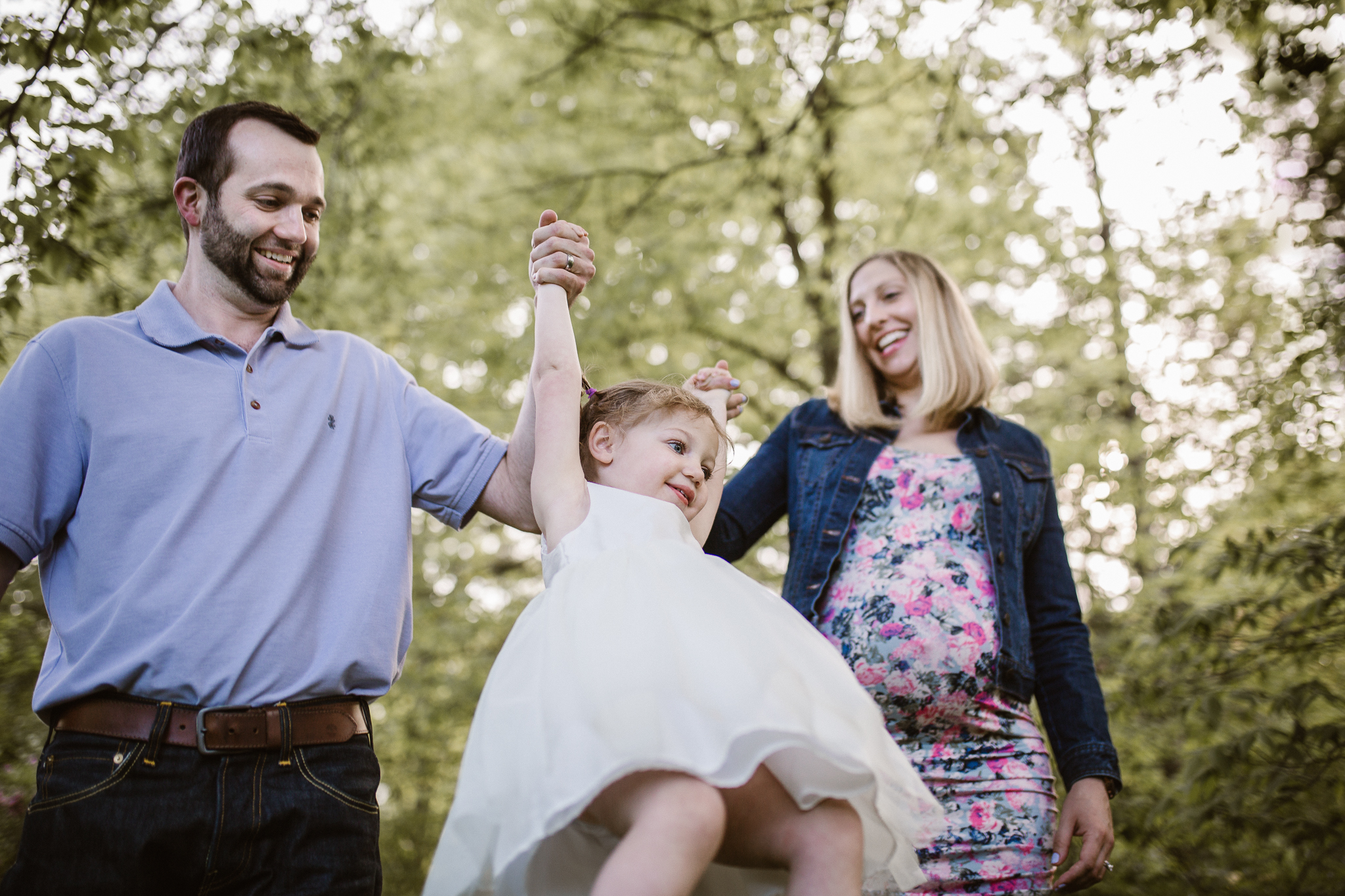 Expecting parents swinging their daughter into the air.