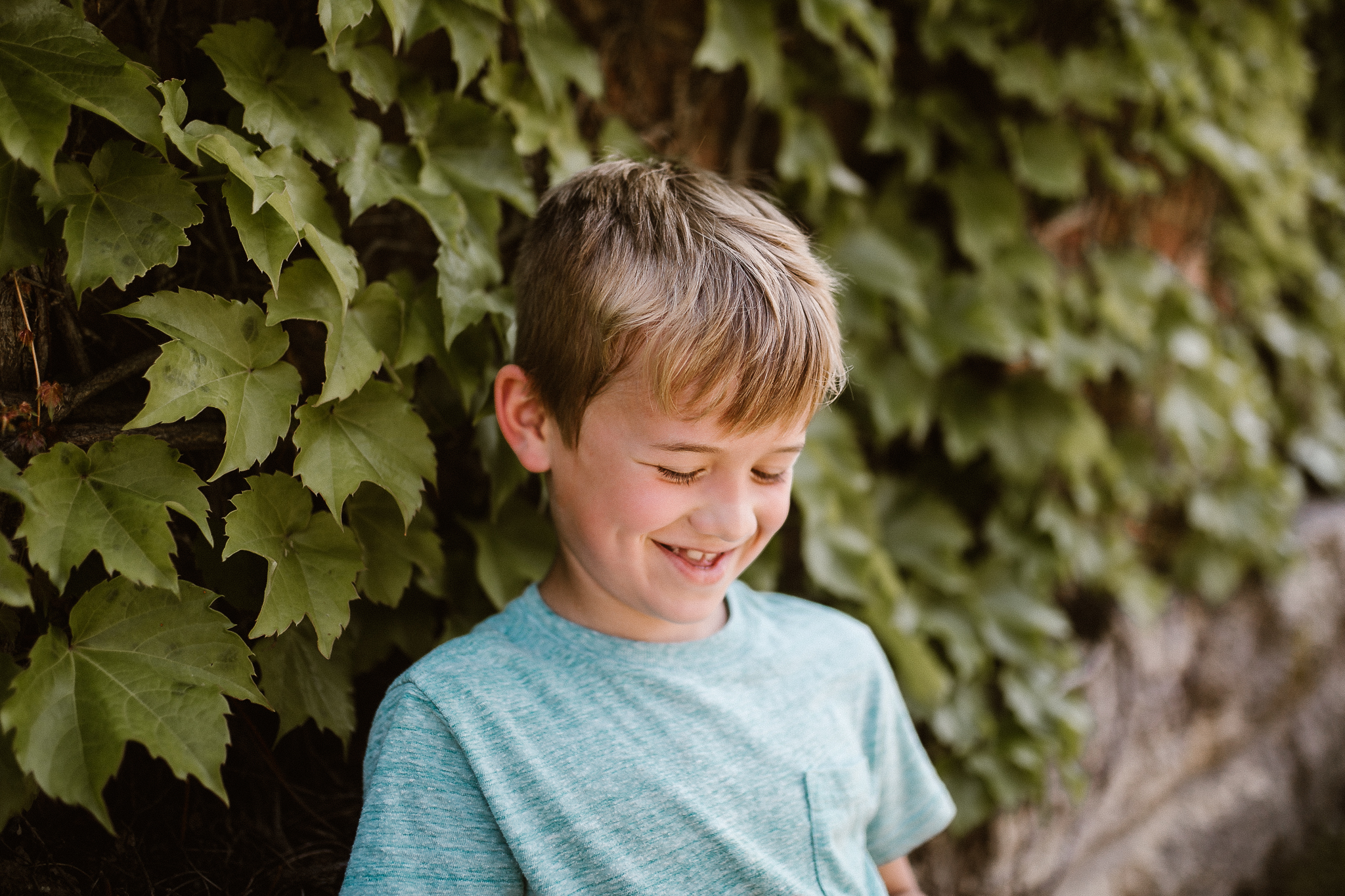 Young boy looking down and smiling in front of an old building with green vines.