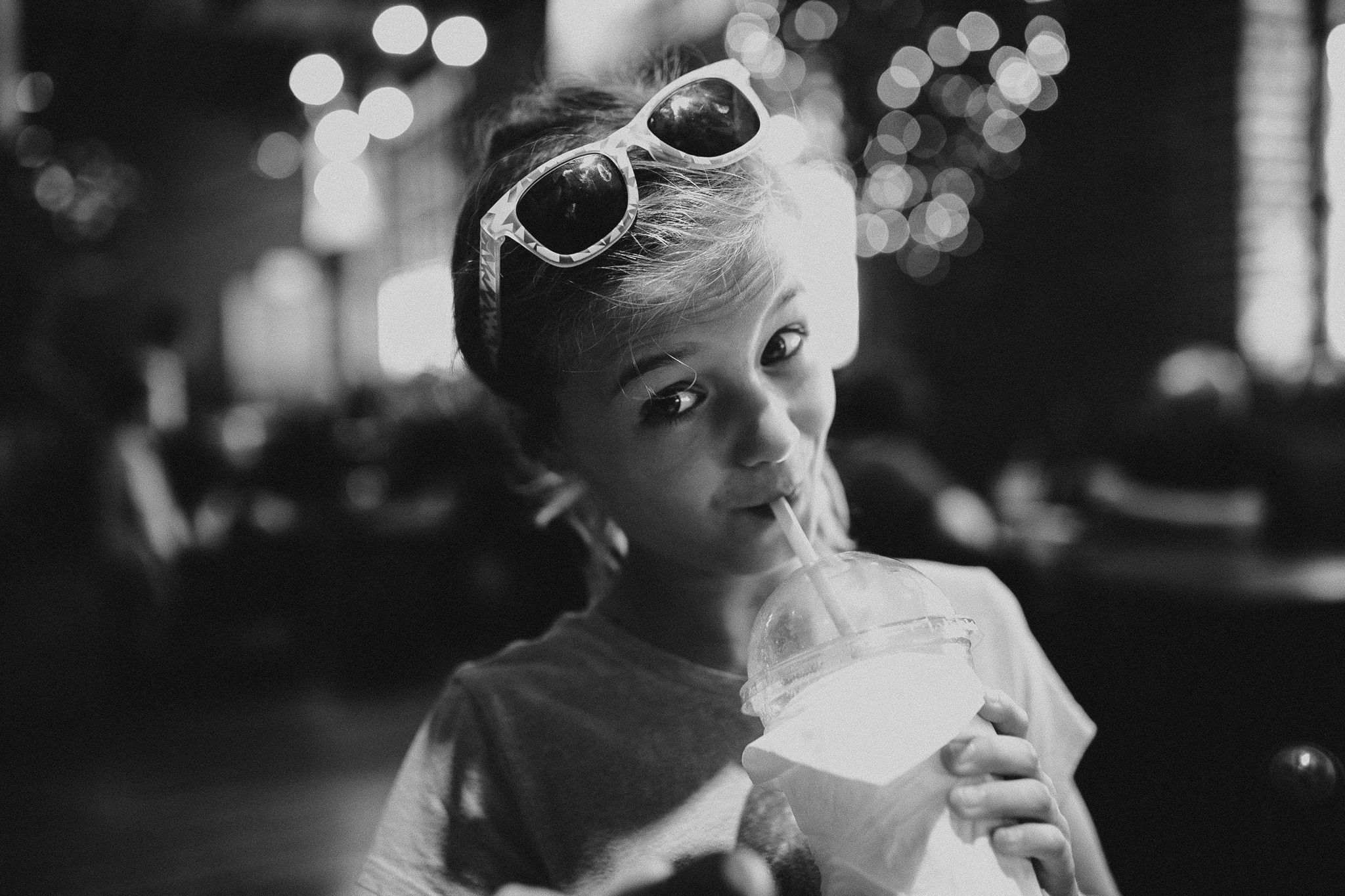 Girl with sunglasses on her head sipping a coffee drink in a lit coffee shop.