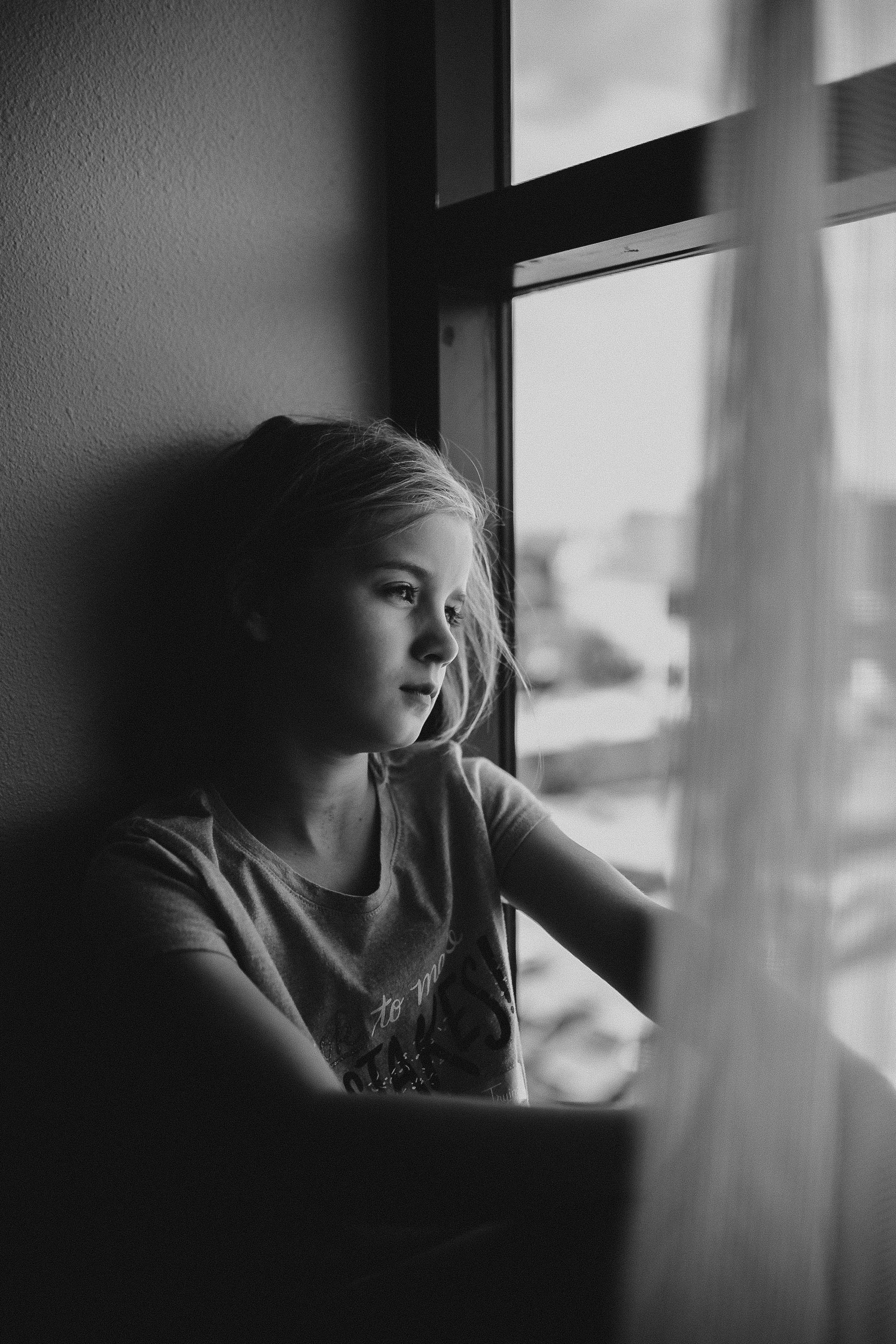 Portrait of a girl staring out the window of a hotel room with moody light.