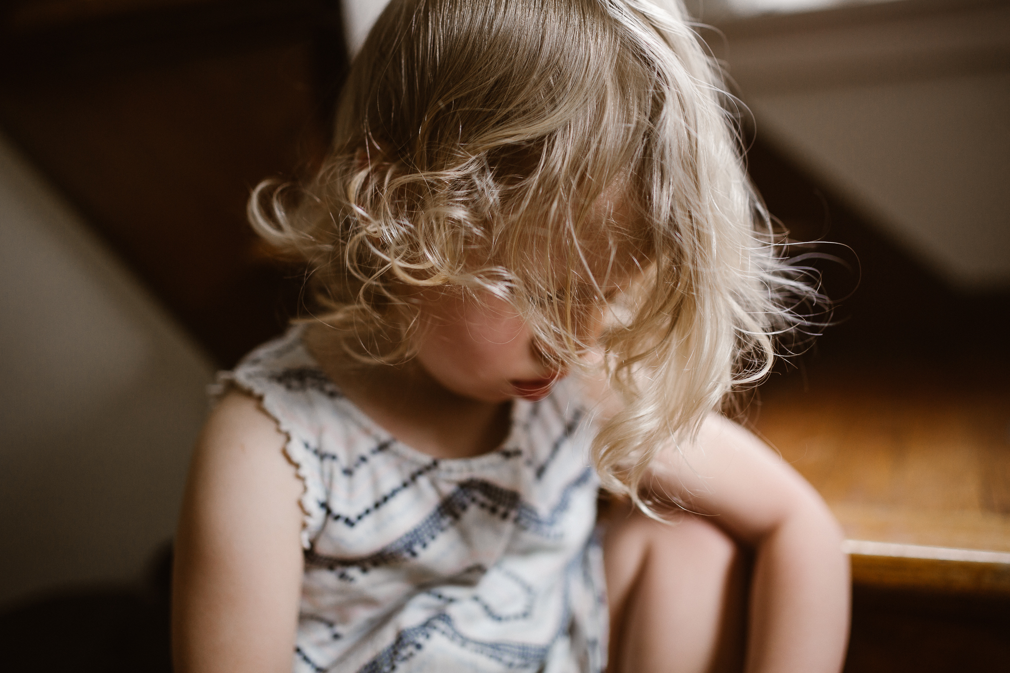 Toddler girl after nap sitting on the step near a window.