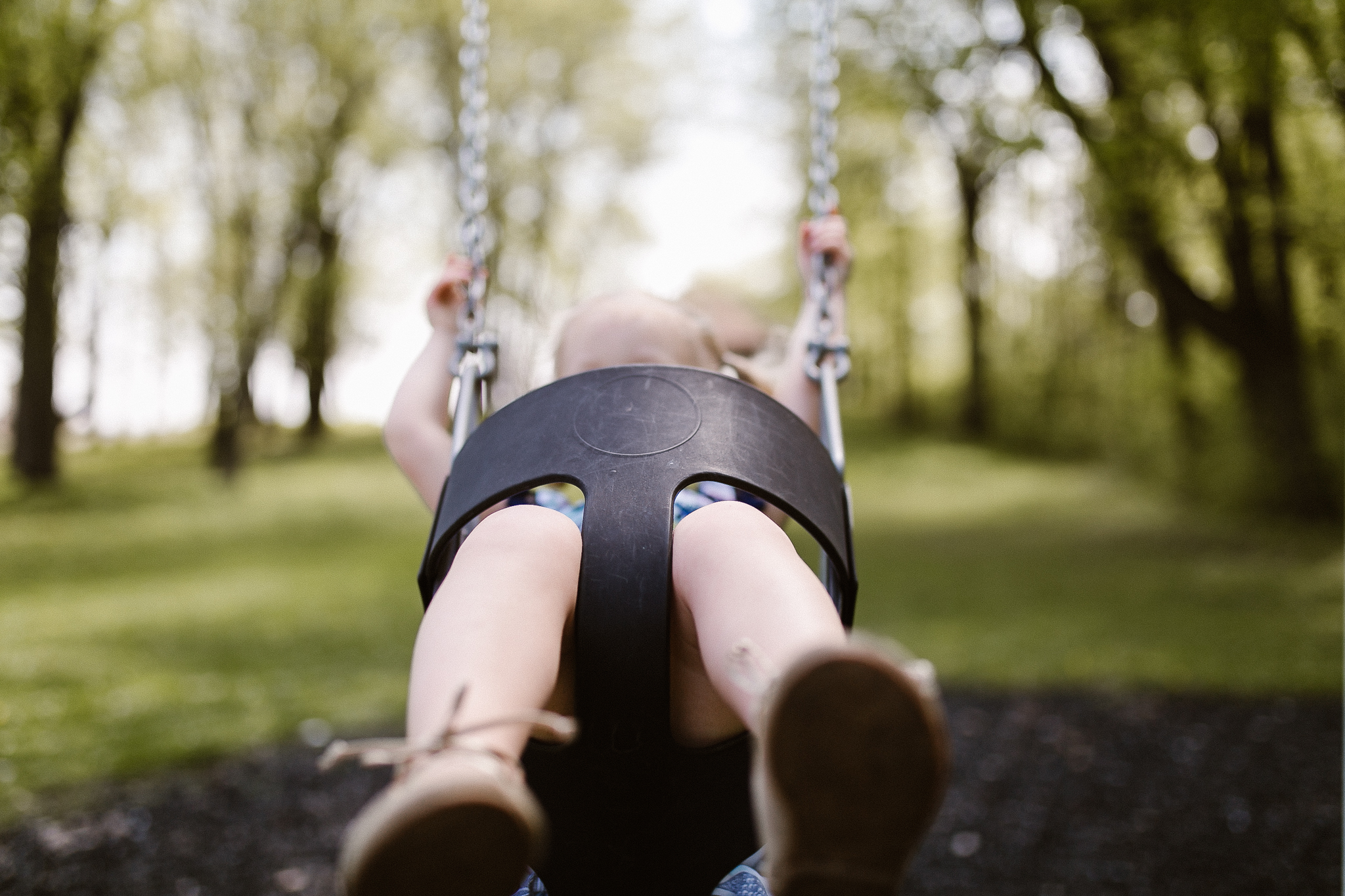 Young girl swinging at the park in the trees.
