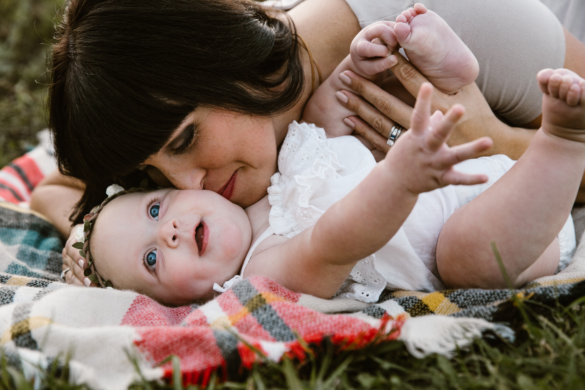 Baby girl laying on a plaid blanket with her mother closely nuzzling her.