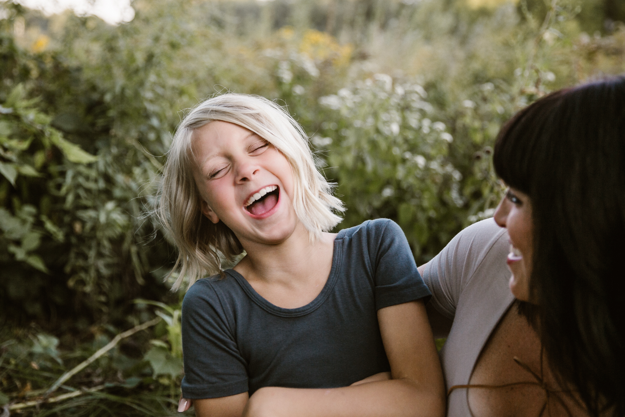 Young girl laughing in a flower field, sitting on her mom.
