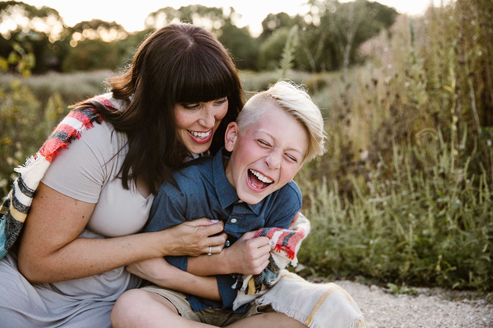 Mother tickling tween son in a flower field at suset.