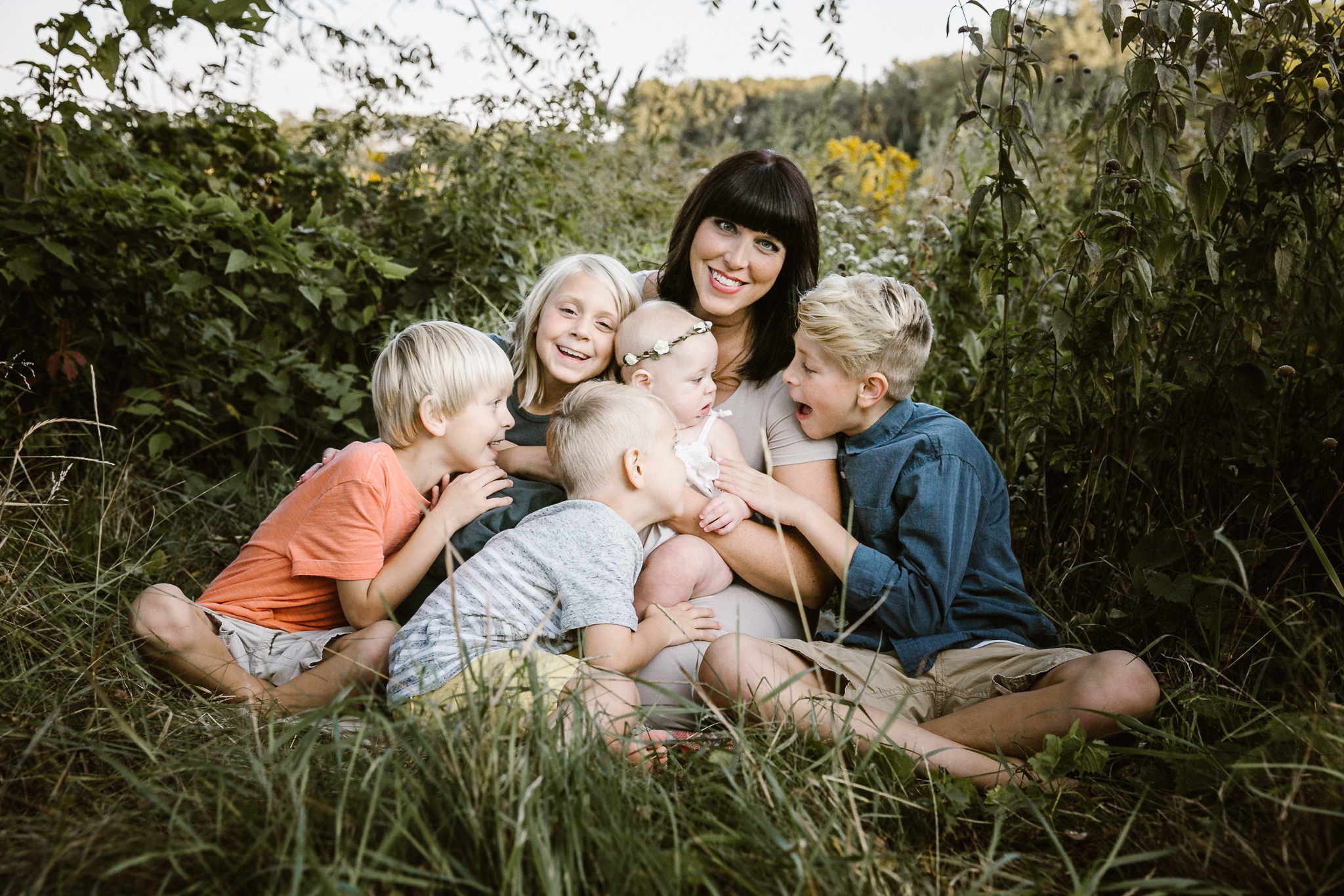 Mother sitting candidly with her five children in a wildflower patch.