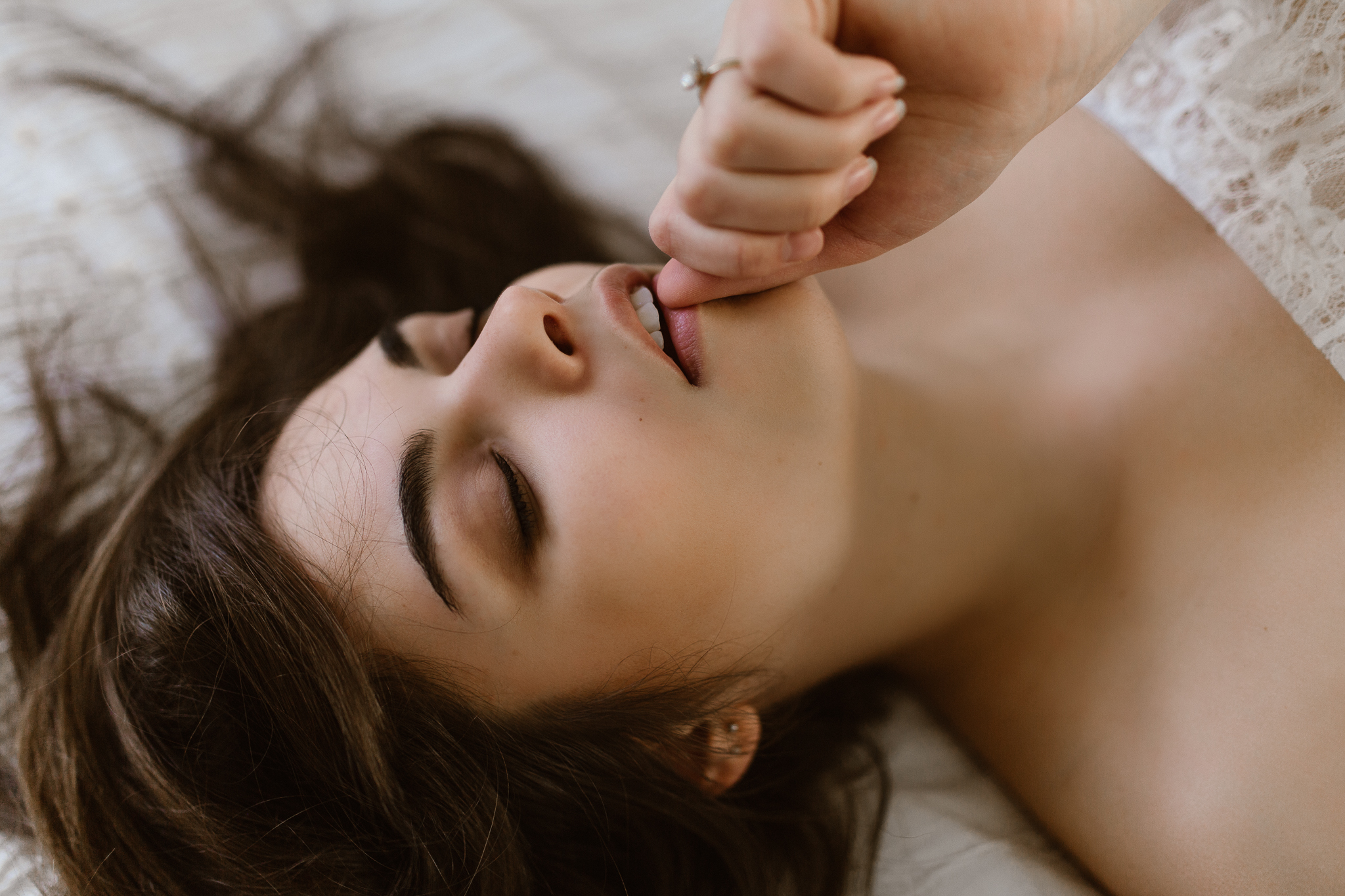 Brunette laying on a bed intimately biting her thumb. Boudoir.