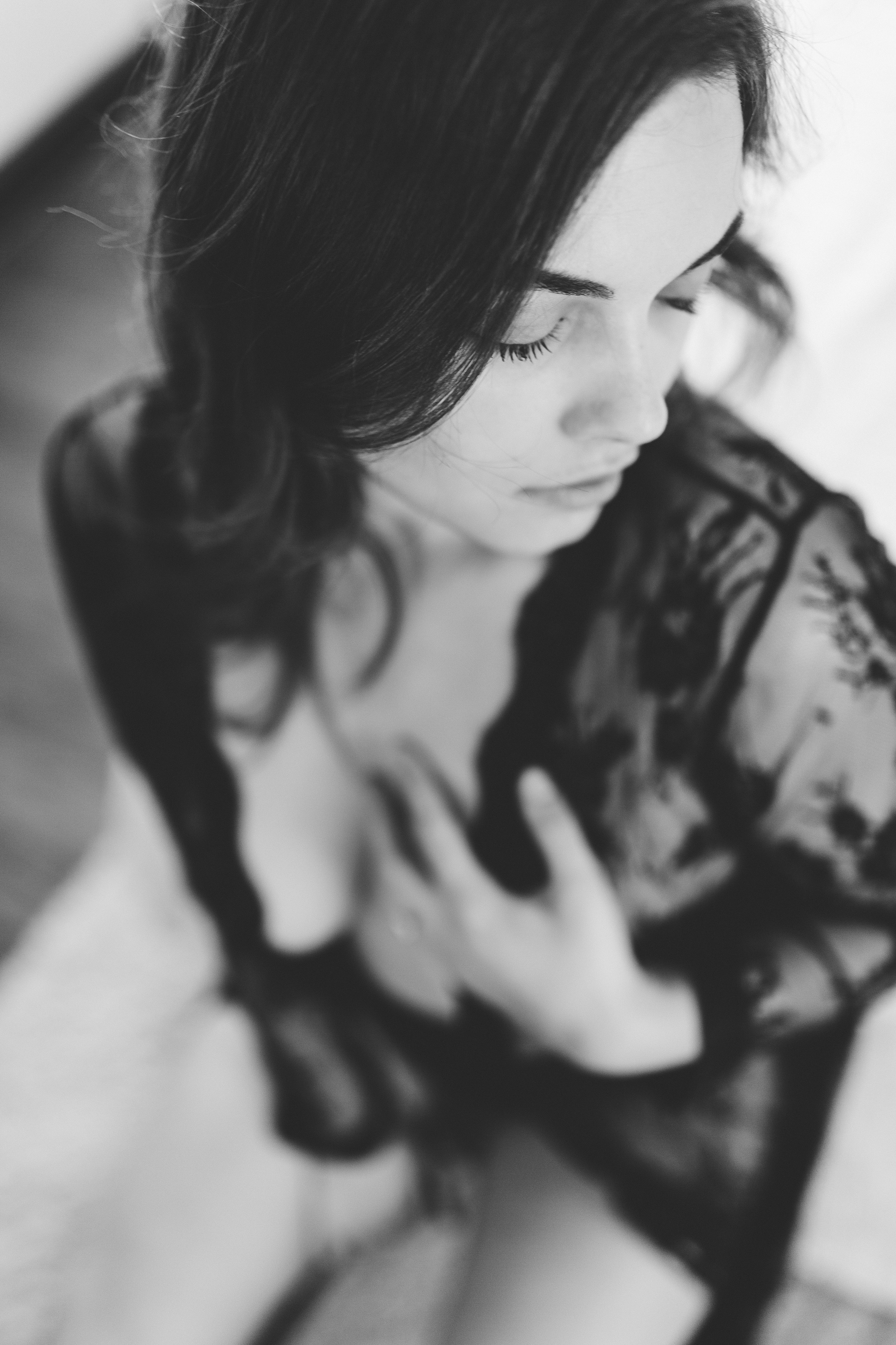 Portrait of a woman in a long, black lace robe, softly touching her chest. Boudoir.